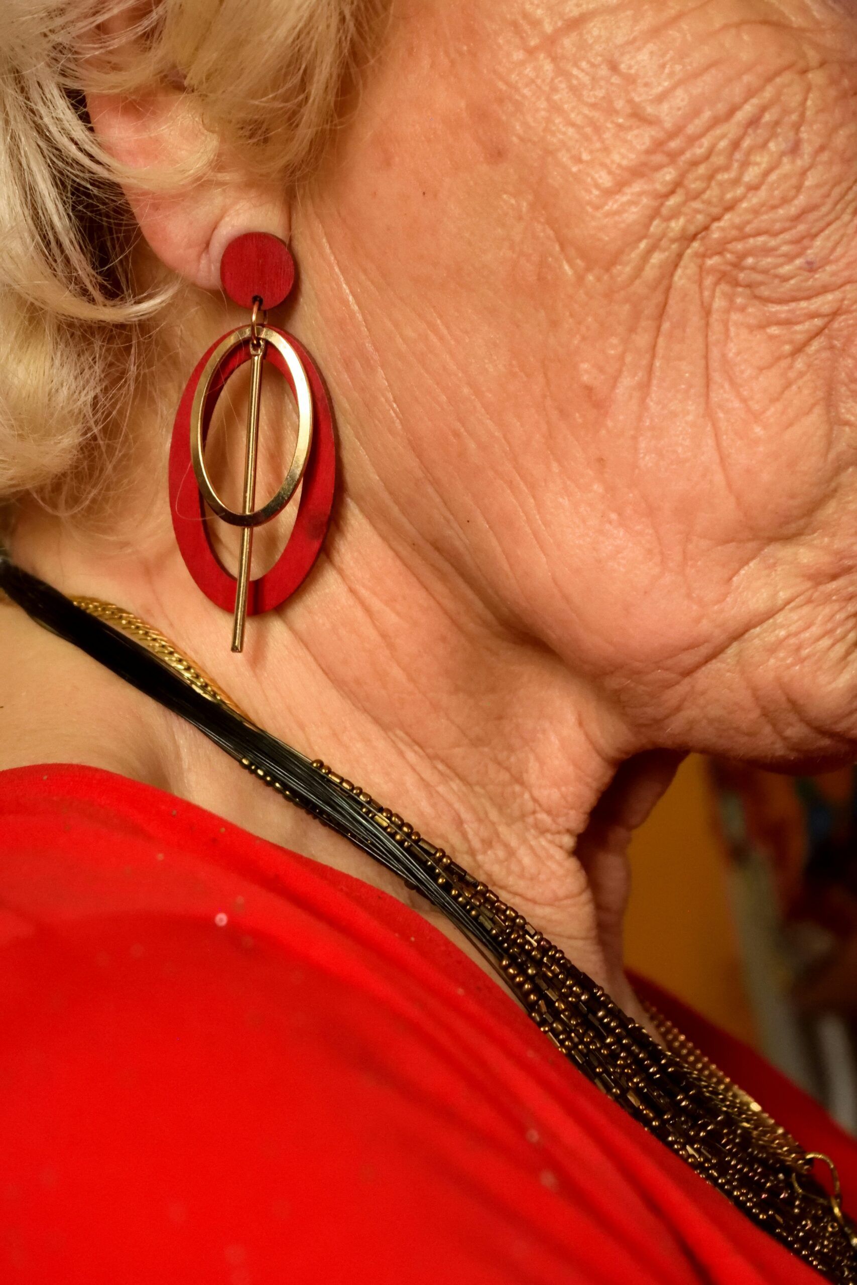 Schönheit einer Oma von der Seite mit Schmuck, rotem Shirt und Falten auf der Wange